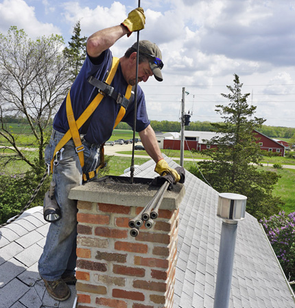 Worker using rods to service a brick chimney on a shingled roof