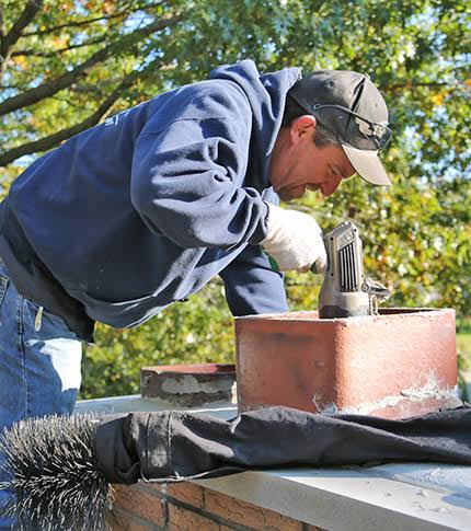 Person using a chimney brush beside a red-brick chimney outdoors
