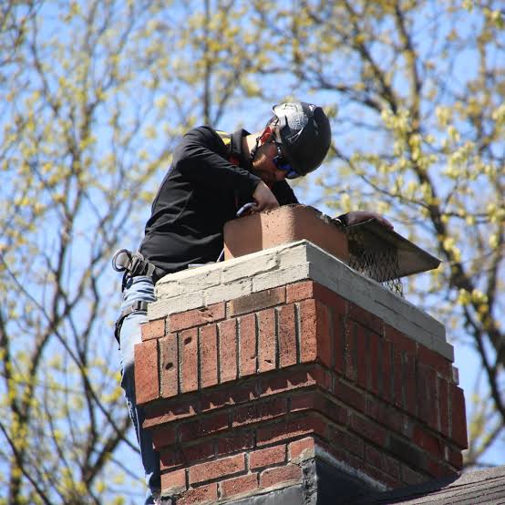 Worker in a hard hat inspecting the top of a brick chimney beside its metal cap